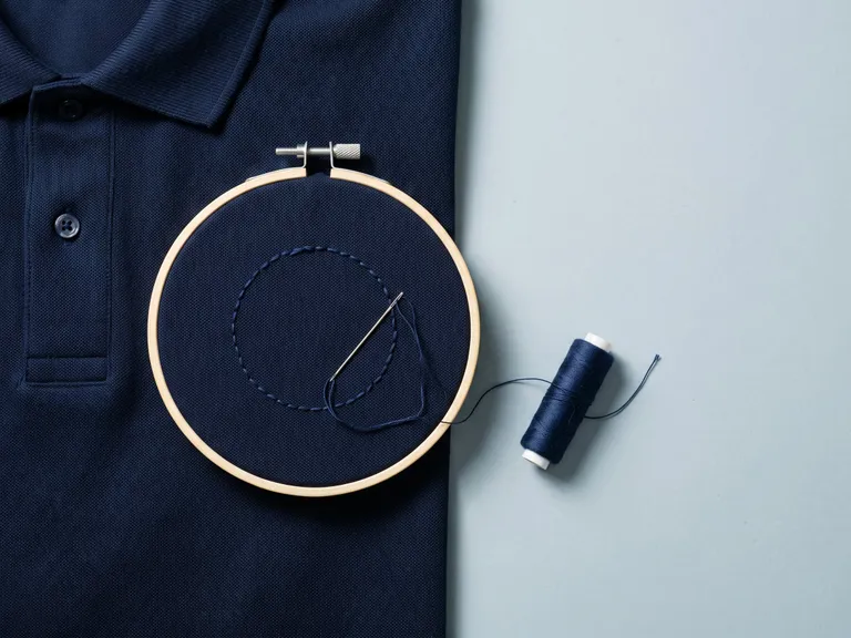 Polo blu sul telaio da ricamo, con il filo per ricamare il logo